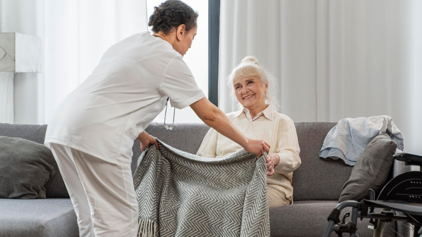Caregiver helping an elderly woman with a blanket in a living room.