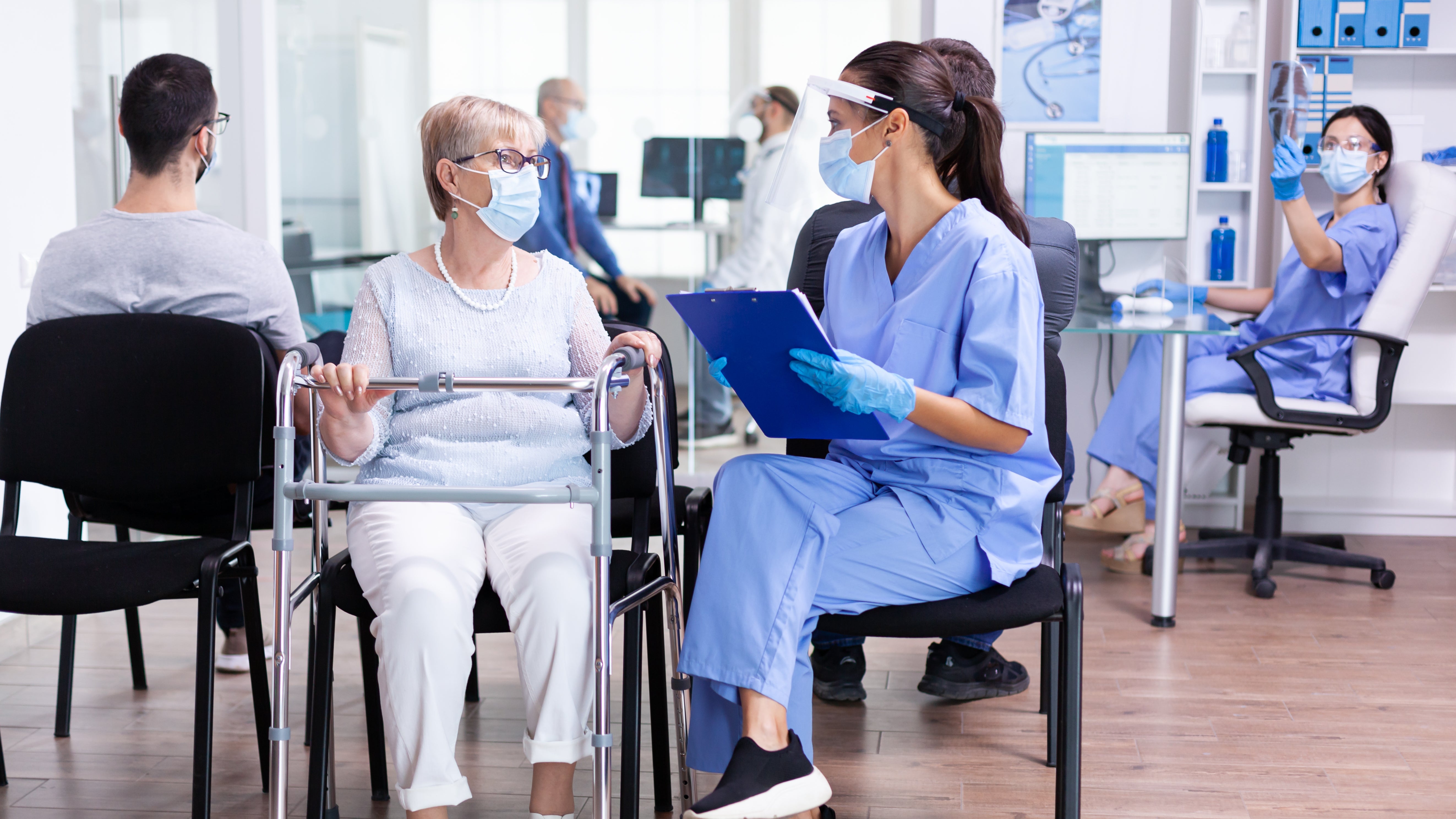 Woman using a walker in a medical setting with healthcare professionals.